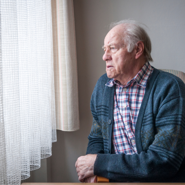 Older man looking outside through window.